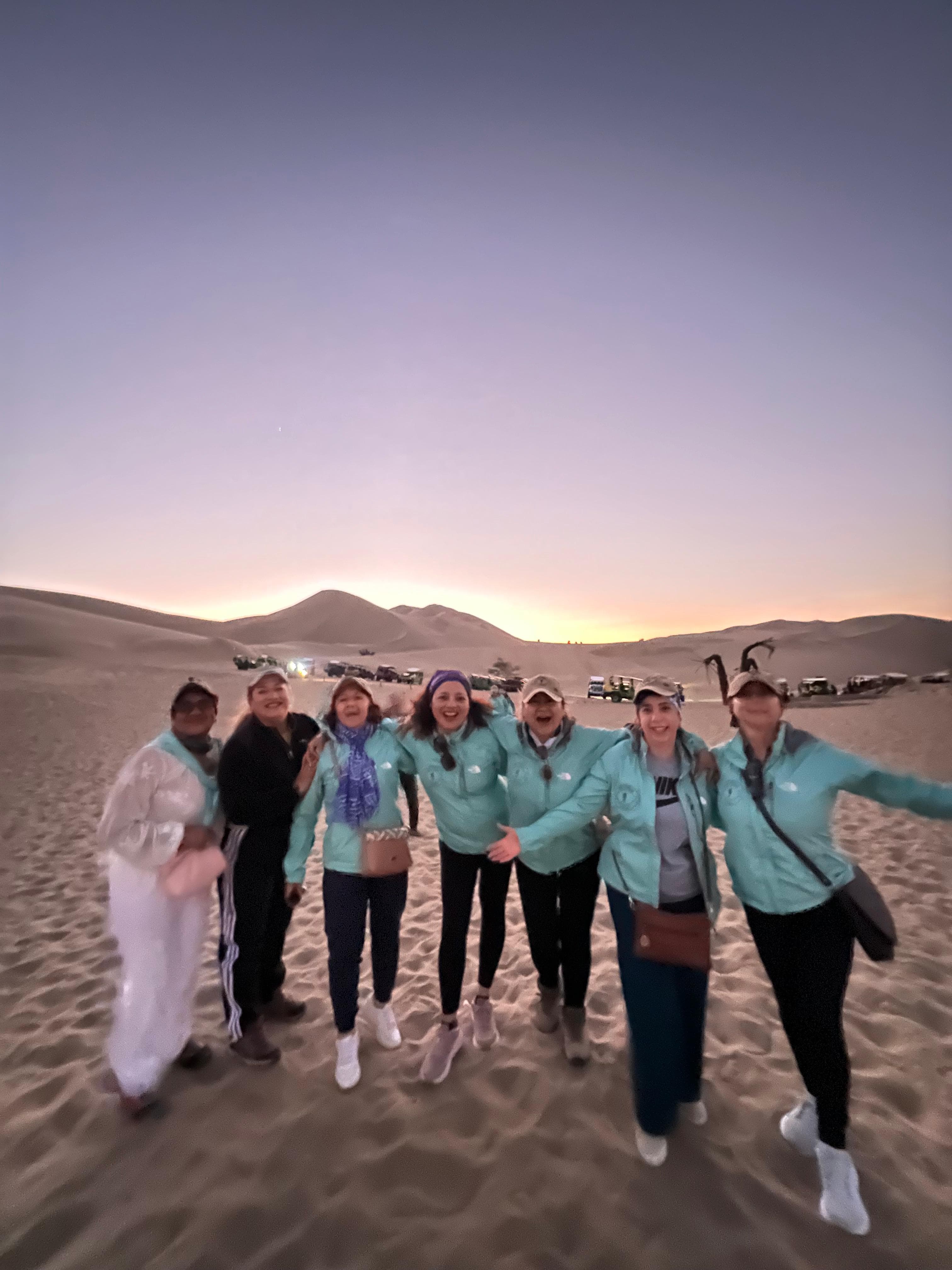 Grupo de andariegas con chaquetas turquesa en dunas al atardecer